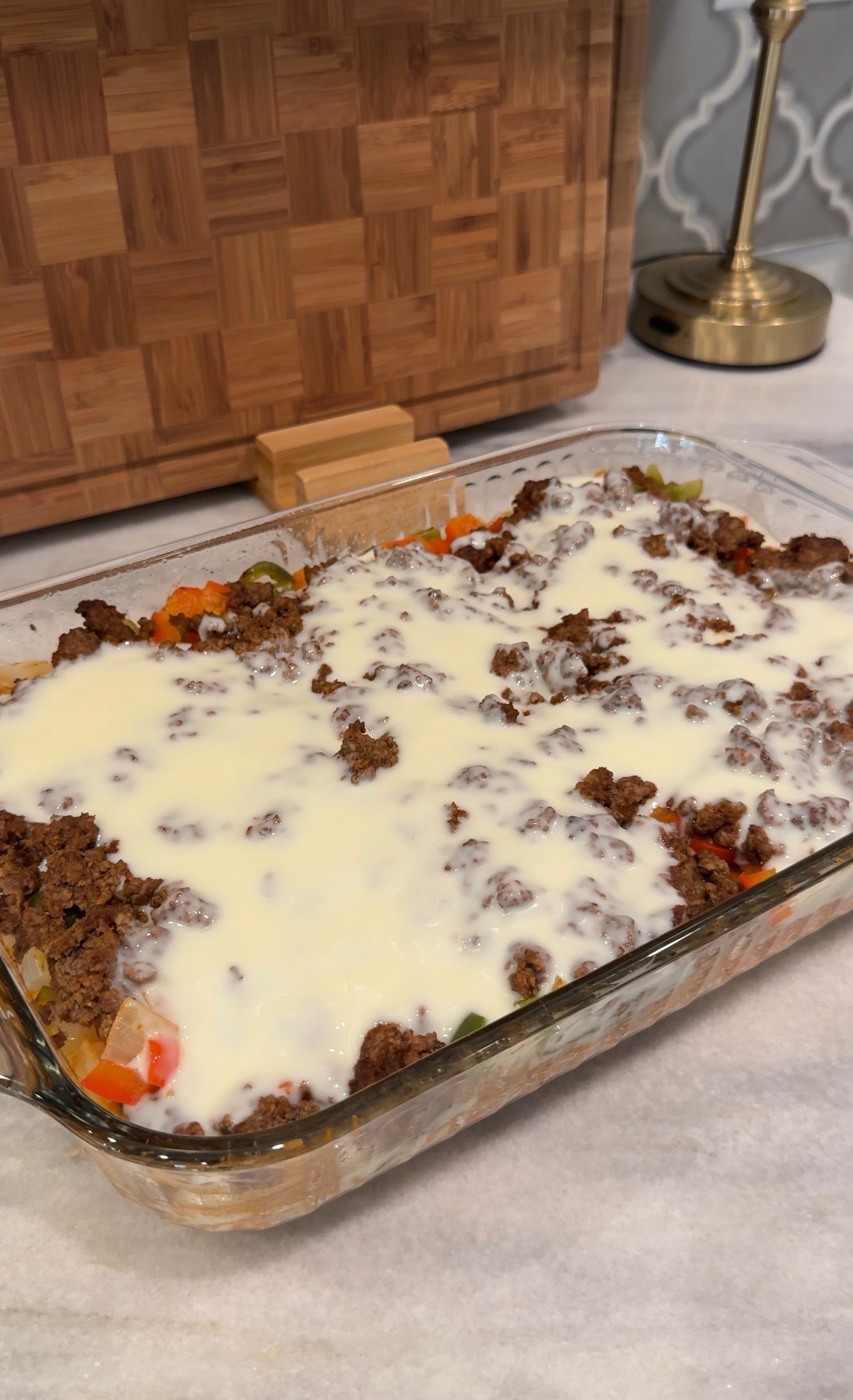 A glass baking dish filled with a casserole topped with browned ground beef and melted cheese, resting on a marble countertop.