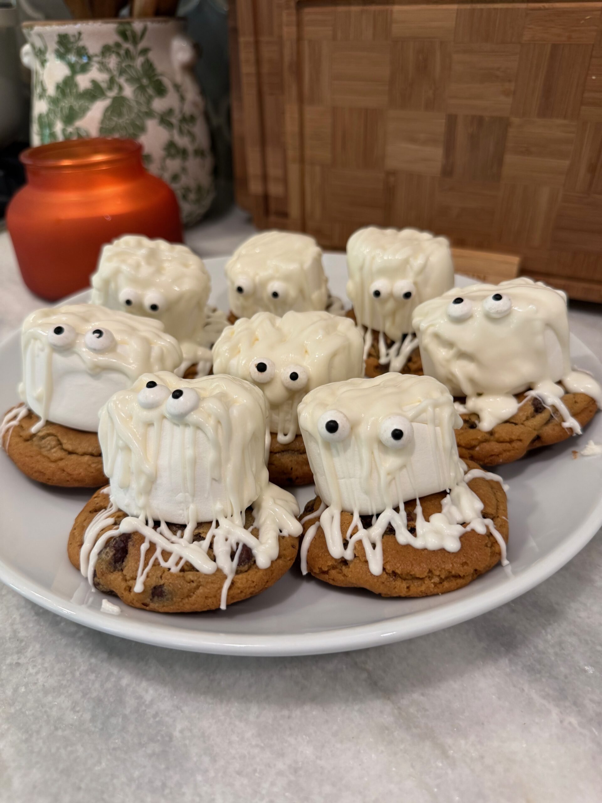 A plate of cookies topped with marshmallows decorated as spooky monsters, featuring drizzled white icing and candy eyes.